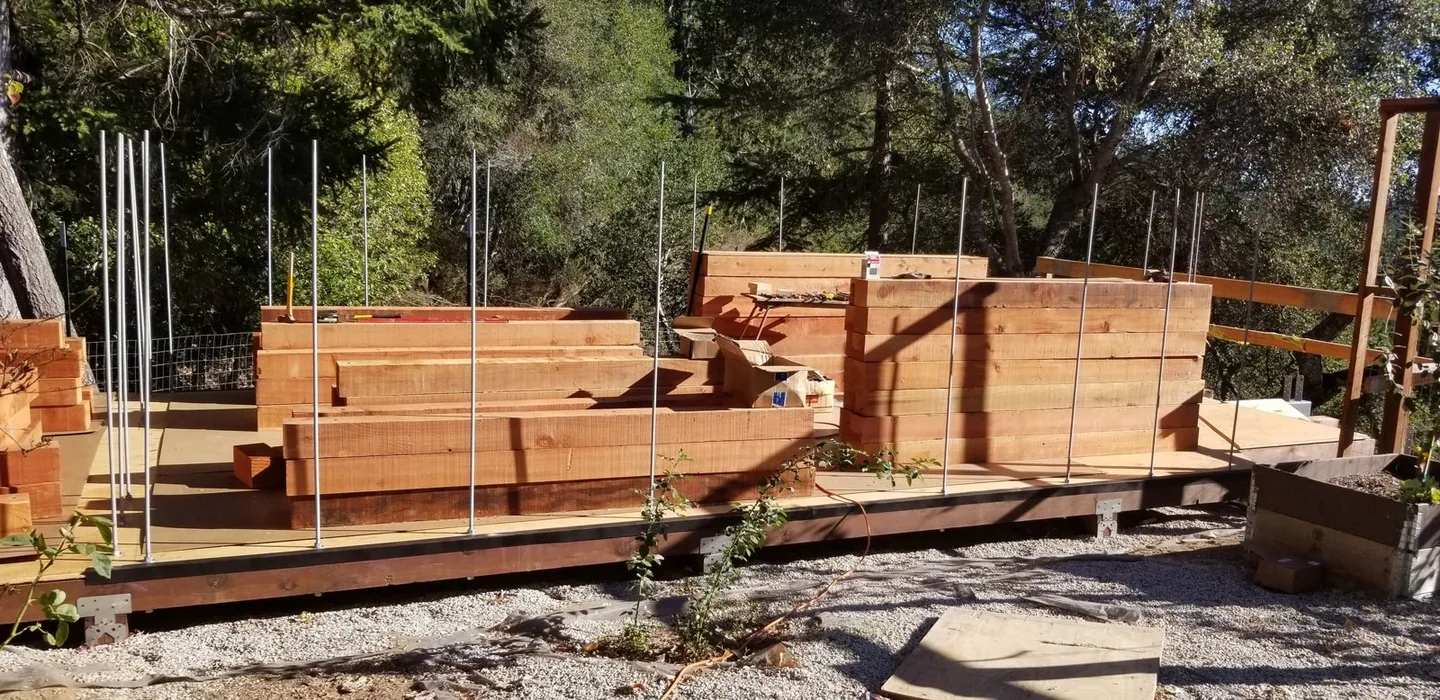 Threaded steel rods standing in the foundation while the first redwood courses are stacked over them at the Falcon's Nest